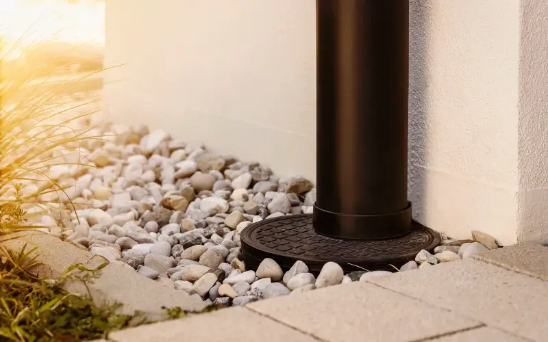 800x450 dark brown gutter pipe attached to a drain in the ground surrounded by gravel
