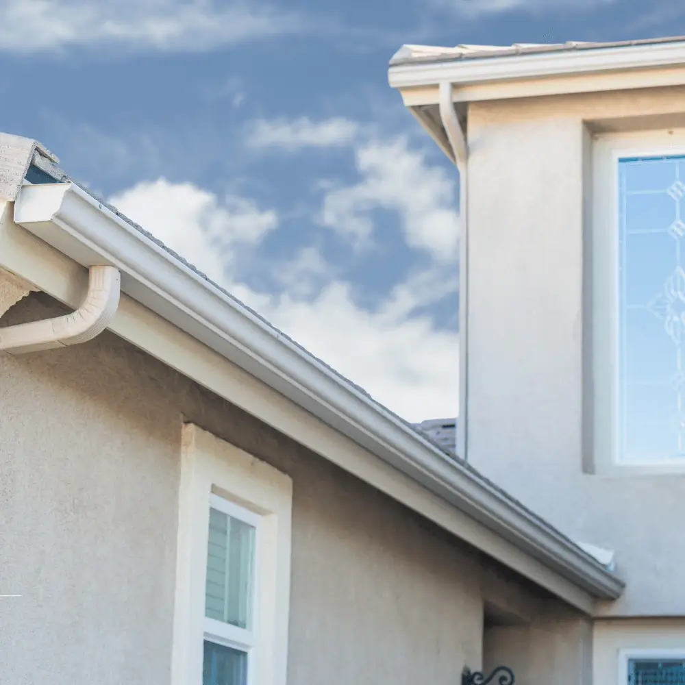 under a blue sky with white clouds a light tan two story home with custom white gutters
