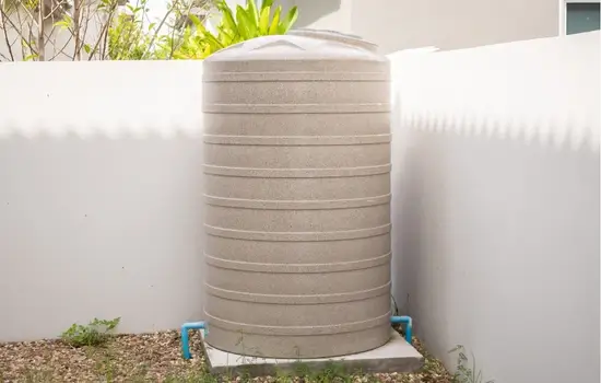 a light tan above ground residential water storage tank sits in the corner of a backyard