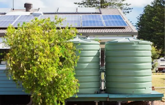 large green above ground commercial water storage tank sit behind a commercial business with a small green leafed tree standing nearby