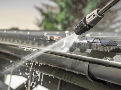 a strong stream of water gushes out of a power washer pointed at a home gutter during the cleanout process