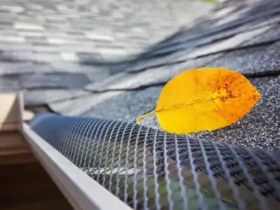 a fall yellow leaf lies atop a dark silver mesh gutter guard showing the efficacy of including gutter guards on a home gutter system
